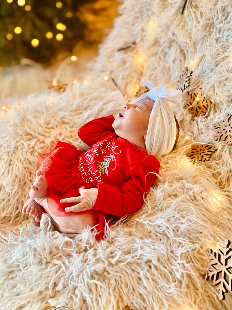 Christmas lights surround  cozy newborn Mosie baby girl in red outfit and white headband